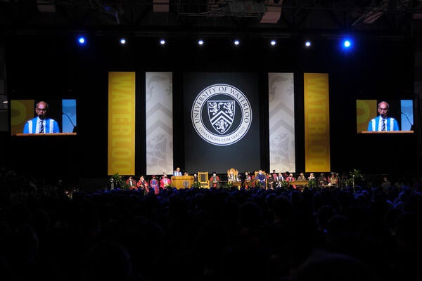 Convocation stage features Vivek Goel at podium and dignitaries seated with the Waterloo crest on a banner behind the stage.