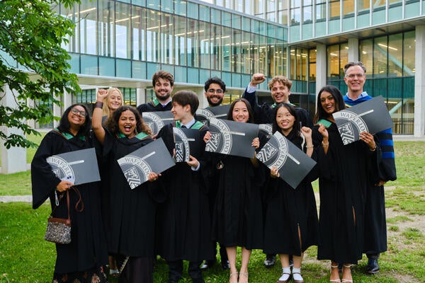 Groyp of SFM gradates in their conovcation robes holding diplomas and celebrating