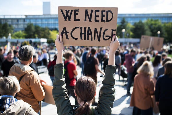 woman holding a cardboard sign that reads "we need a change"