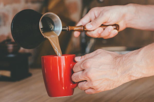Man with jezve pouring latte into red mug.