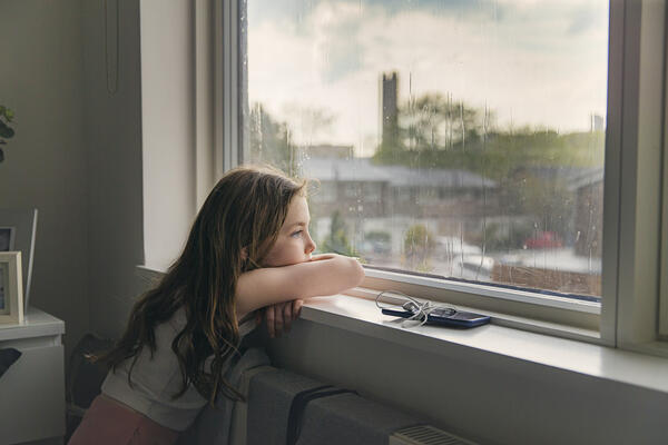 Young girl looking out of window on a rainy day 