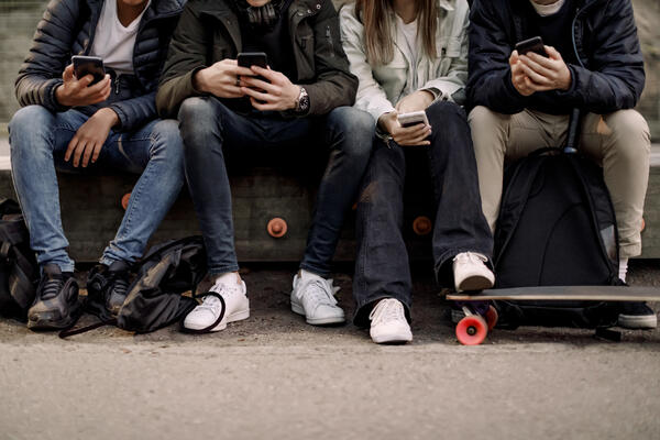 Teenagers sit on their cell phones at the park