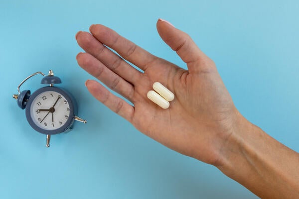 A clock beside a hand with pills 