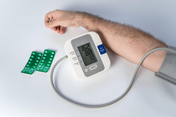Man's arm with device for taking blood pressure and pills