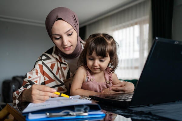 Photo of a mother studying while her child is in her lap. 