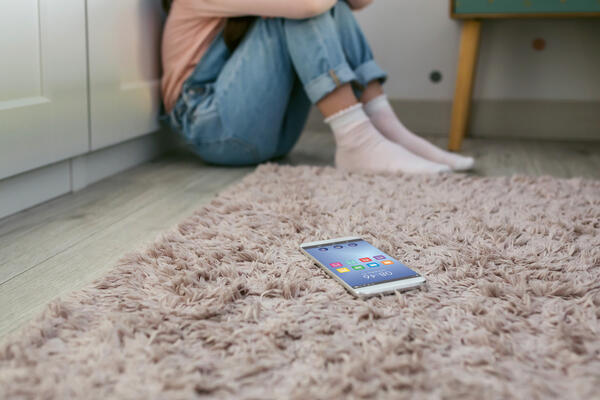 Mobile phone lying on the floor with unrecognizable person sitting behind.