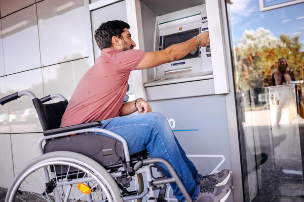 Young person with disability taking out money from an ATM.