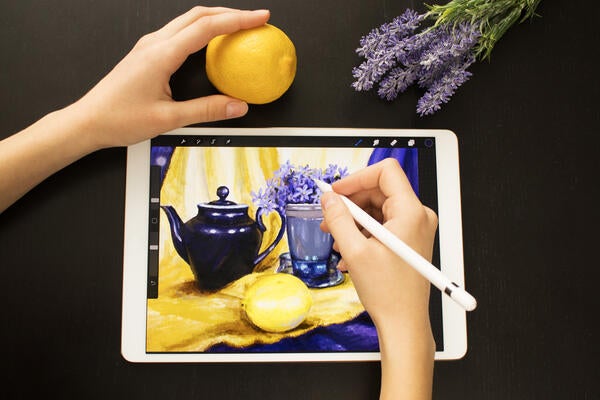 Someone draws a still life picture with teapot, lemon and flowers with a pencil on an electronic tablet.