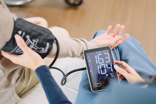 A nurse checks the blood pressure and heart rate of a woman as both sit on a bed.