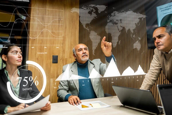 Team of executive leaders pointing at a hologram of the world map