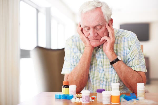 Senior man sitting and looking at his medication despondently