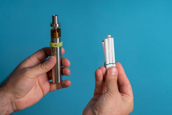 A person's hand hold e-cigarette while the other holds regular cigarettes 