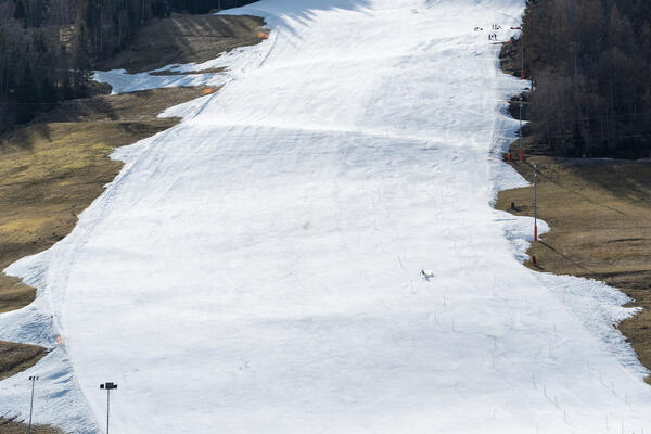 Skier slaloms on hill with snow and grass
