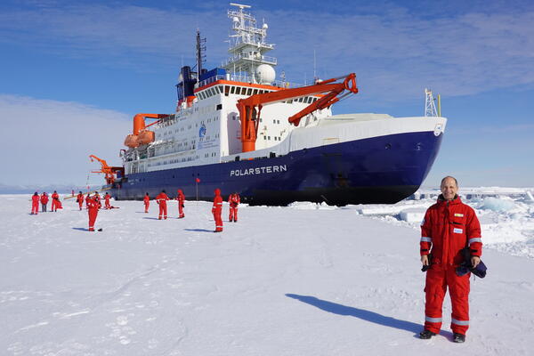 Gotz Hoppe standing on Antarctic ice flow in from of ship