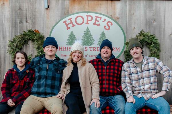 The Hope family sits together on a log with a barn behind them