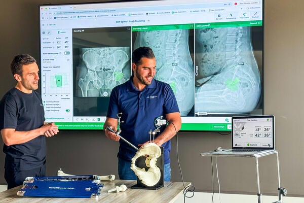 Two research use sensors while examining a pelvis in front of a wall of xrays
