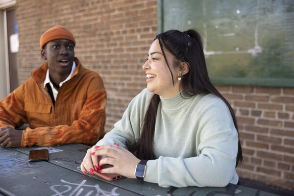 A Black young man and a white young woman talking at a table
