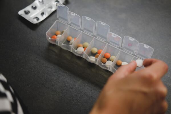 A person putting pills into a weekly organizer that already has several pills in each slot
