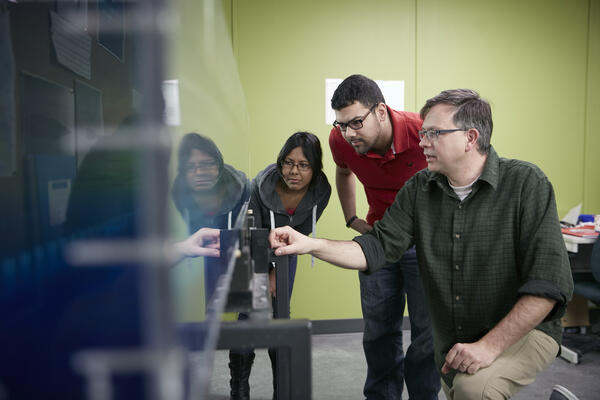 Students examine a machine with their professor