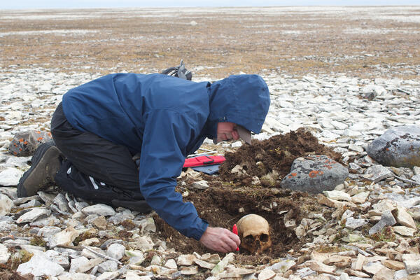 Man using small hand tool to excavate a human skull from the ground