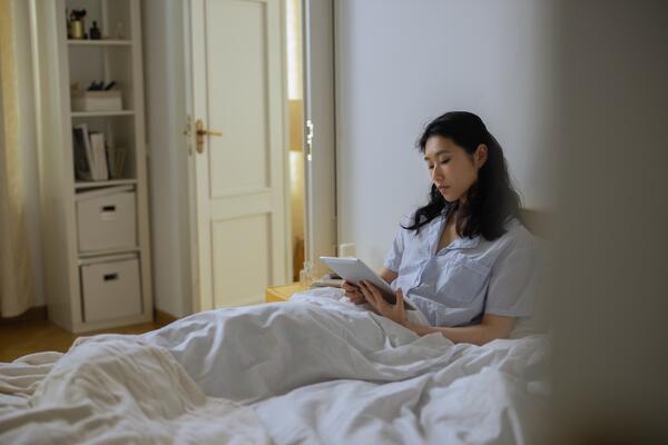 A female lying in bed with a tablet looking at a tablet