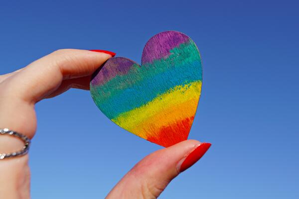 hand holding heart shaped wood peice with rainbow colours