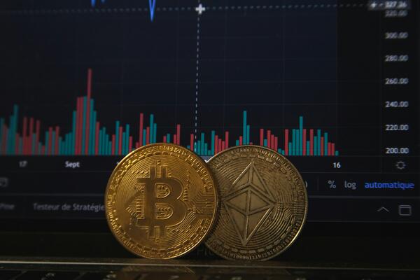 Bitcoin and Ethereum tokens in front of a computer screen with financial data