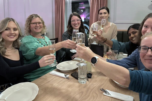 The five team members and two instructors hold up glasses around a table