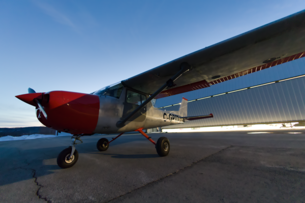 Small red and white plane parked at hanger