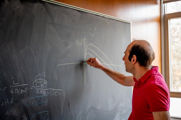 Man uses chalk to draw lines on a blackboard