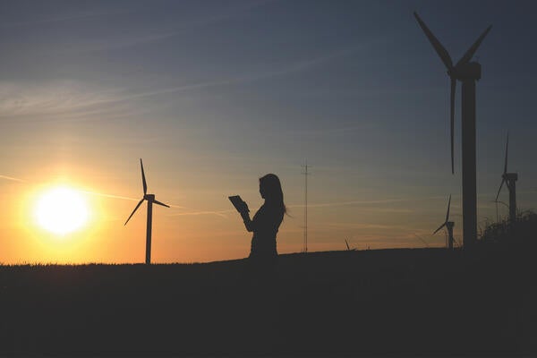 Someone reading with windmills and the sun in the background 