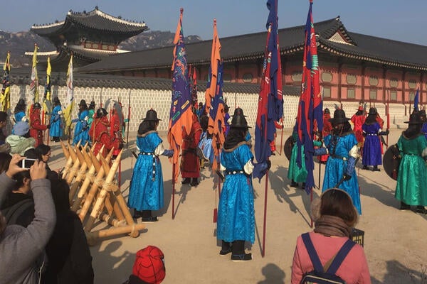A photo taken in South Korea of people standing in bright coloured robe holding large flags.