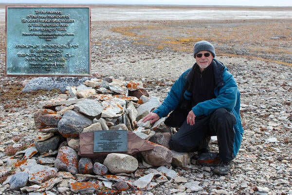 Dr. Douglas Stenton kneels beside a plaque honouring those lost in the Franklin expedition