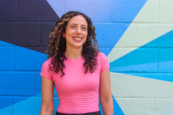 Artist Stephanie Boutari stands in front of a colourful mural and smiles