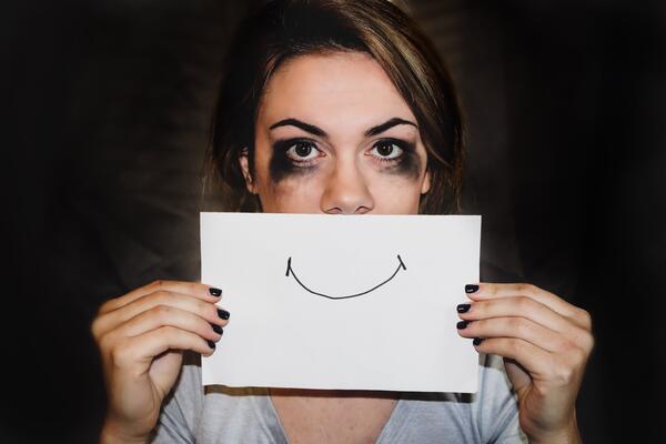 Woman with smudged mascara on her eyes holding a piece of paper with a smile that covers her mouth