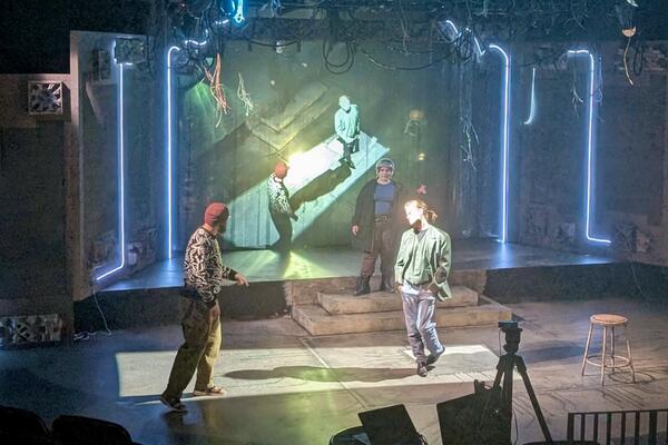 Three people rehearsing on a stage with a VR projection on screen behind them