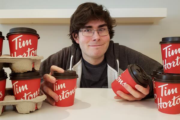 Michael Wallace, a white man with glasses, poses with several Tim Hortons cups