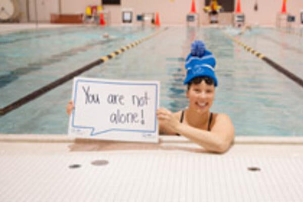 Waterloo varsity swimmer holding sign that reads "You are not alone"