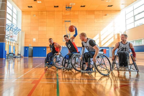 A group of four male athletes play wheelchair basketball on an indoor court.