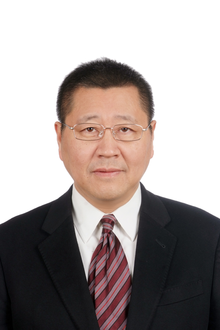 Weiya Xu stands square facing the camera, wearing light framed glasses with red tie, white shirt and black suit jacket