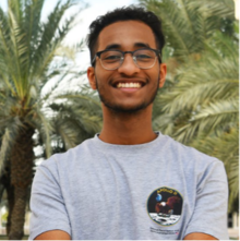 Mohamed Yousuf wearing a grey t-shirt and dark framed glasses, smiling at the camera