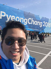 Yishu Meng smiles in front of Pyeong Chang Olympic sign.