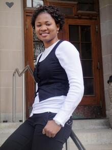 Rita Orji leaning on a railing in front of stone building