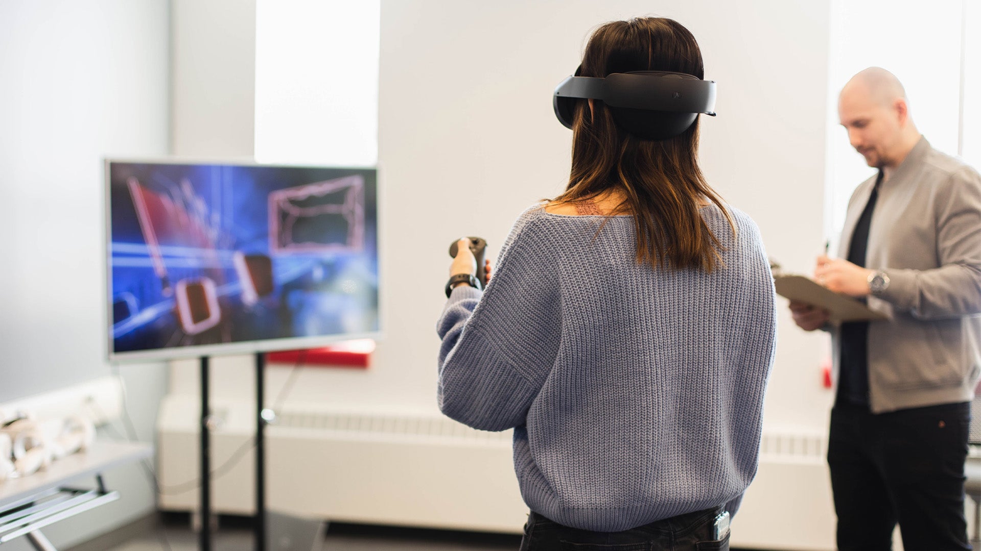 Ville supervises a student using VR equipment whose view casts onto a TV screen