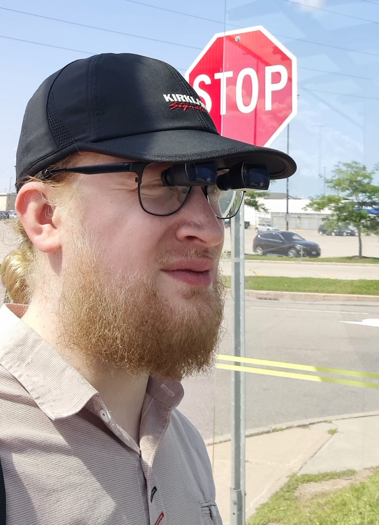 A man wearing spectacle-mounted telescopes standing on a sidewalk