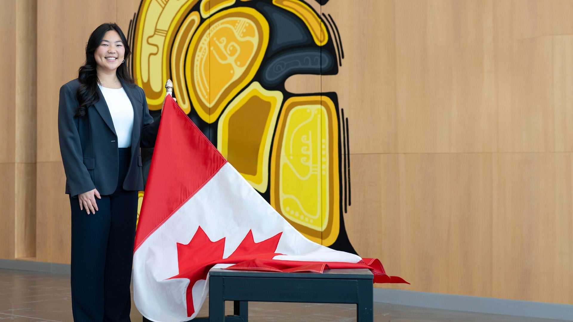 Diane Choi holds up a Canadian flag while standing in front of the Warrior's Indigenous logo