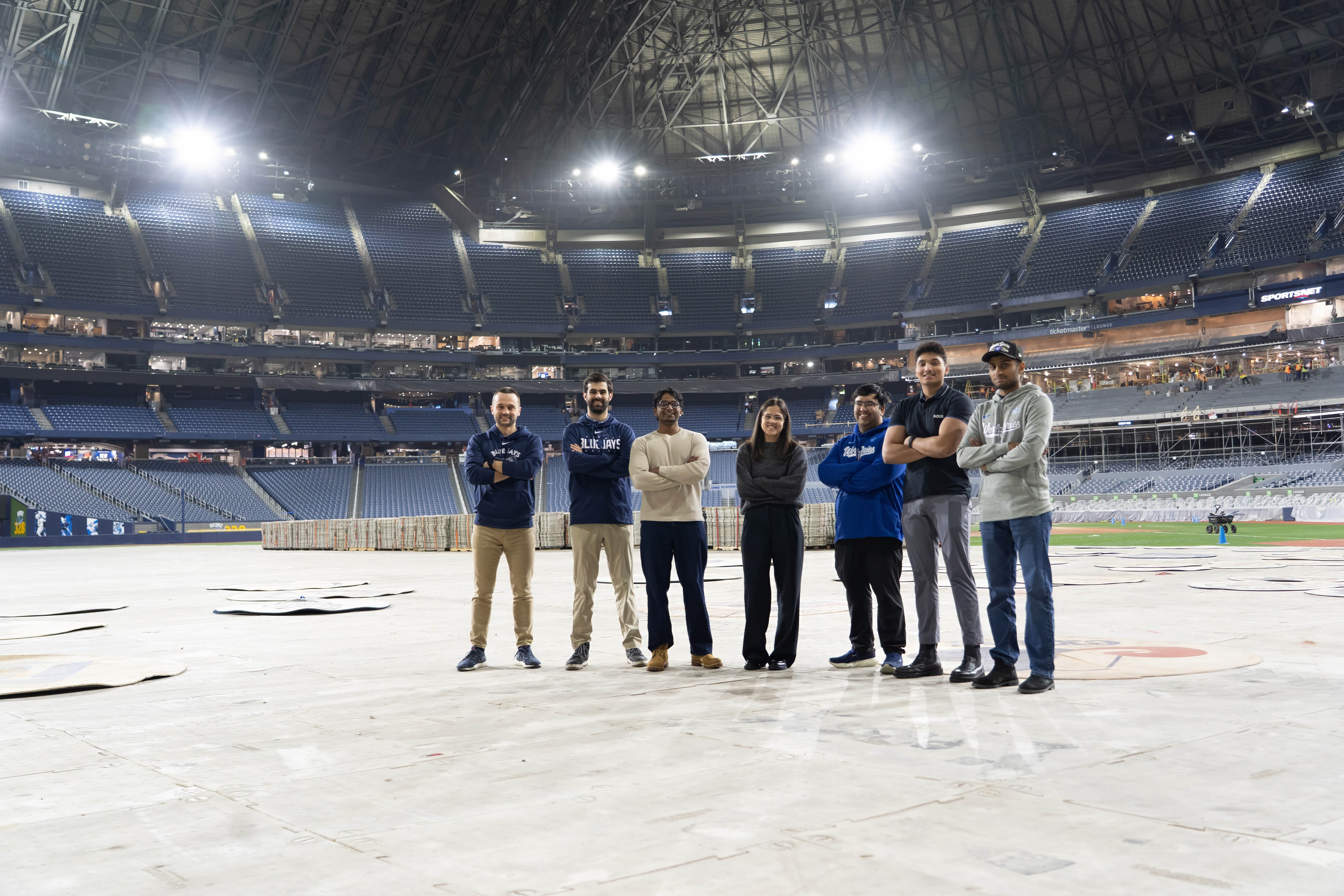 Group of Waterloo alumni pose while standing on tarps inside Rogers Centre