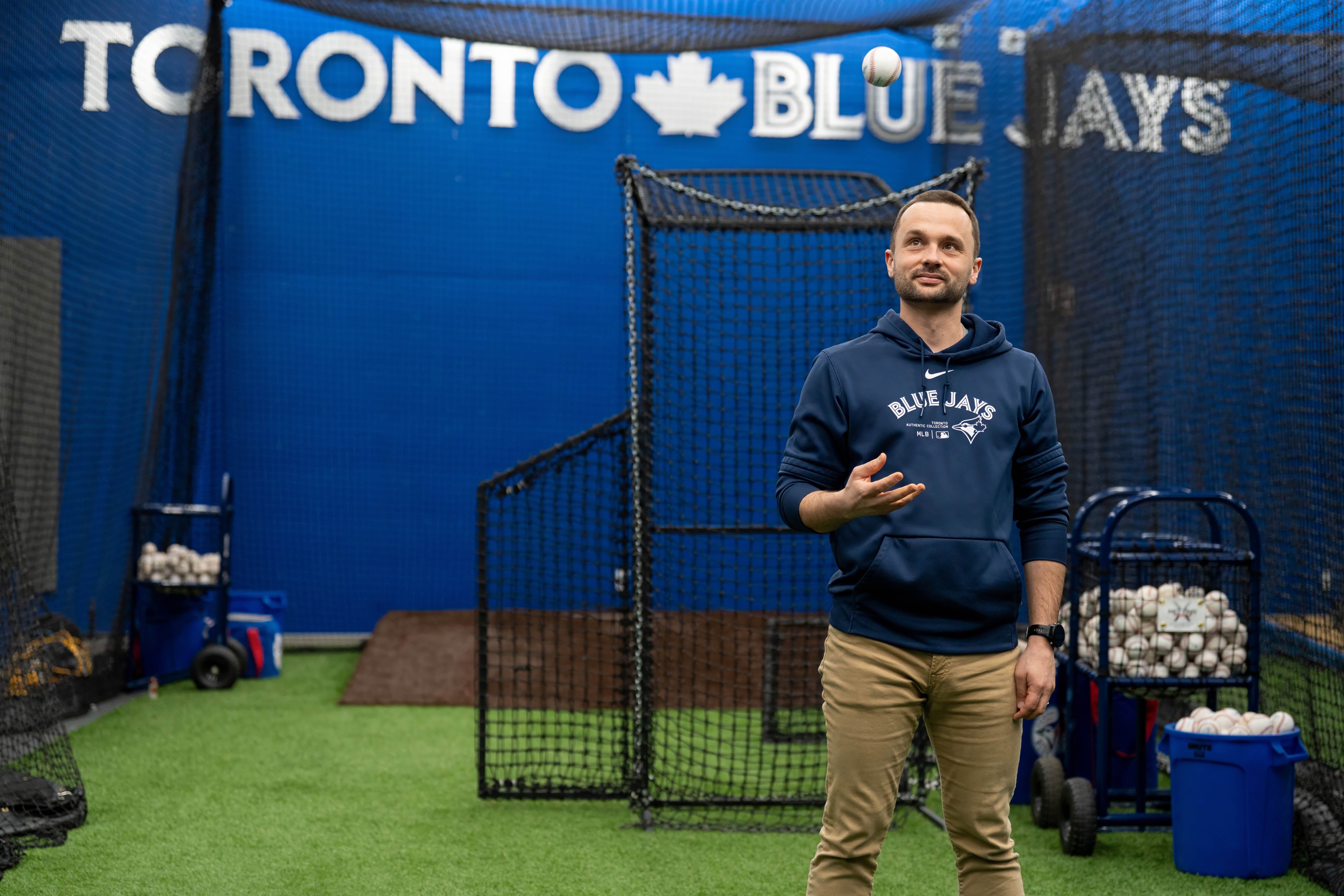 Jeremy Reesor tosses a baseball in the air while standing inside an indoor batting cage at Rogers Centre