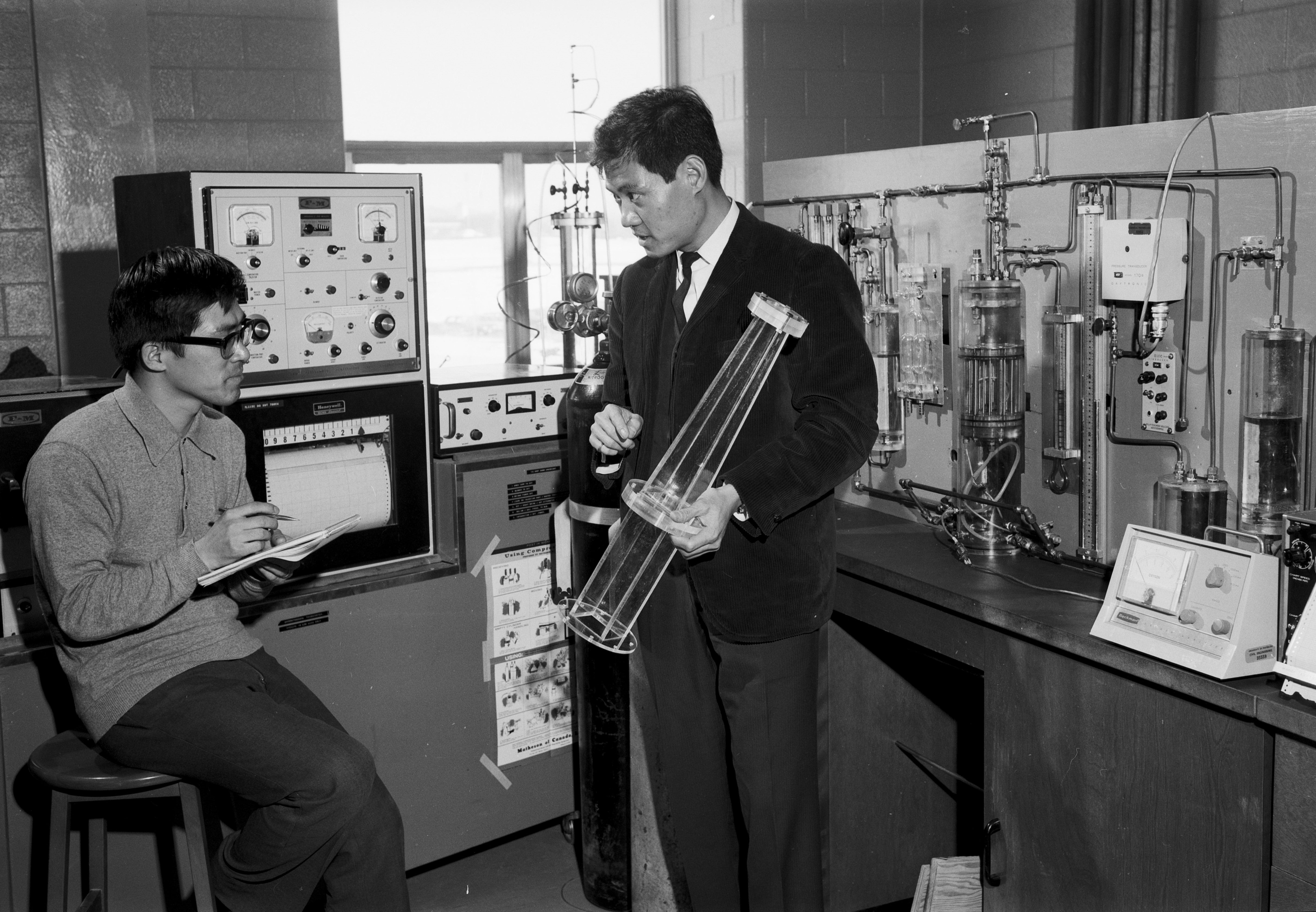 A professor teaches a student in his lab. The student takes notes.
