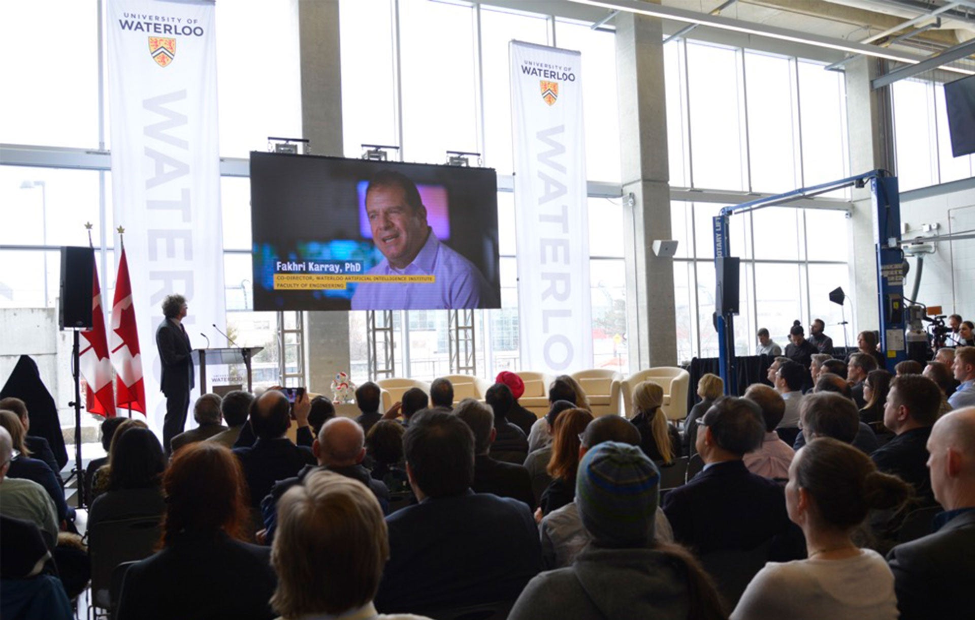 Stephen M. Watt speaks watches a video in front of a large audience at AI Institute Launch
